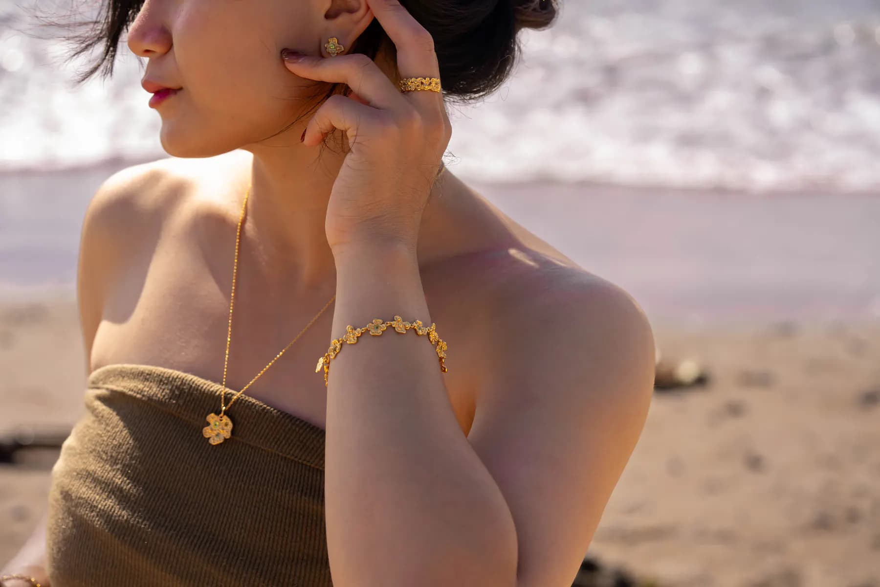 Woman on the beach touching her ear, wearing a flower pendant and floral bracelet