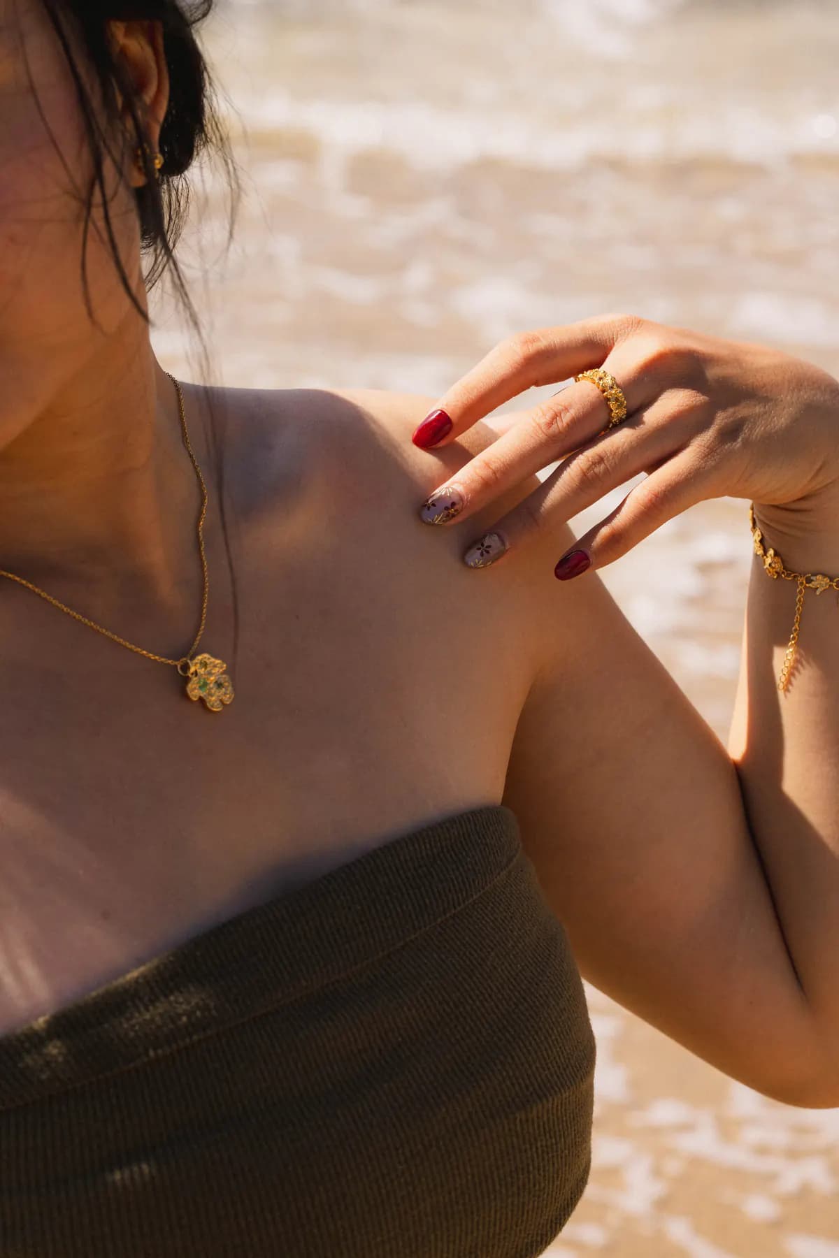 Hand on shoulder showing a gold flower pendant and ring against the surf