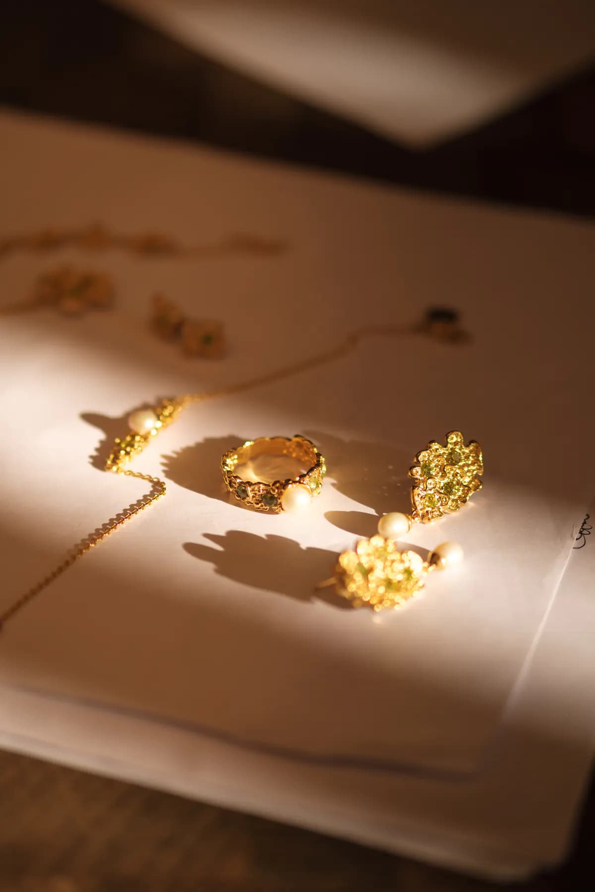 Gold floral ring, earrings and chain on white paper in a sunbeam