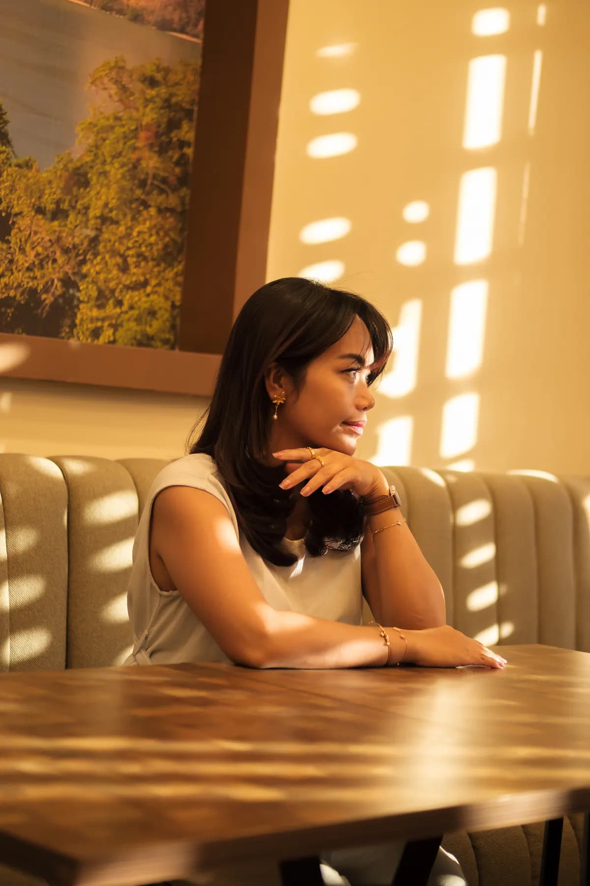 Woman at a sunlit café booth table wearing gold earrings and a ring