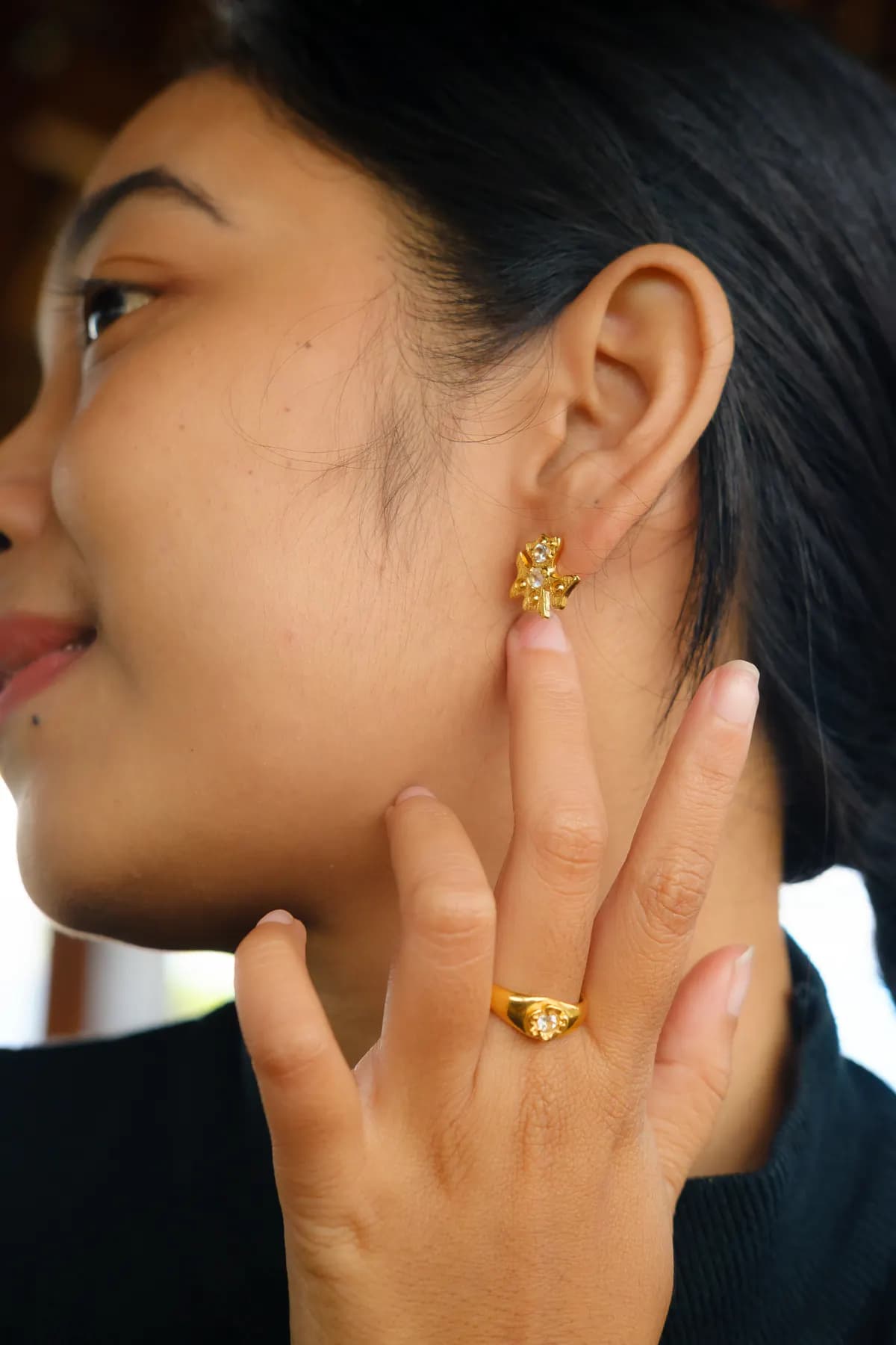 Close-up of a woman touching a gold flower earring, wearing a gold ring