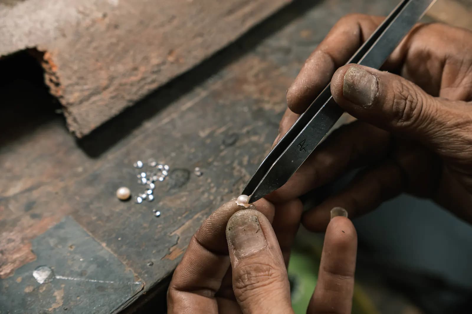 Tweezers setting a small stone into a ring, loose stones on the bench