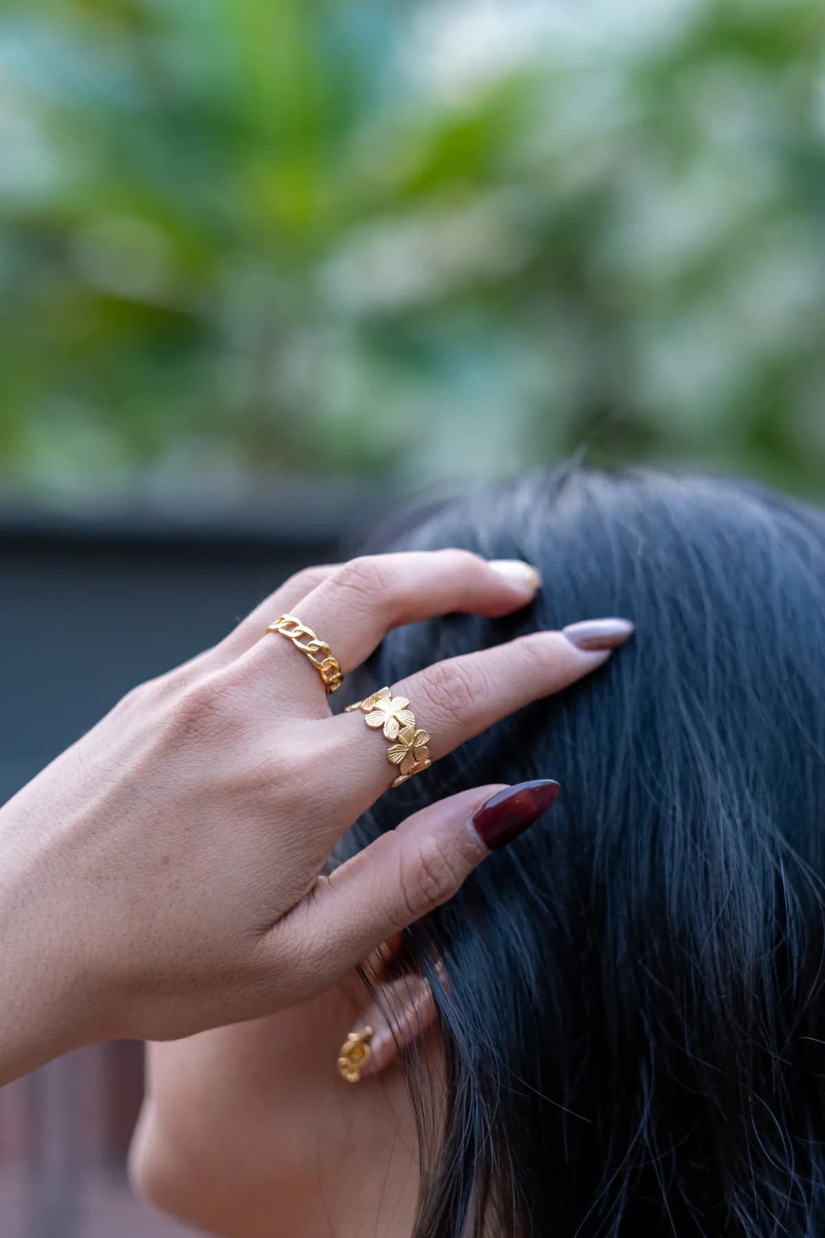 Hand with gold chain and flower rings running through dark hair