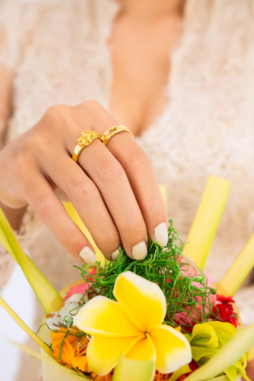 Hand with gold floral rings placing a frangipani into a canang sari offering