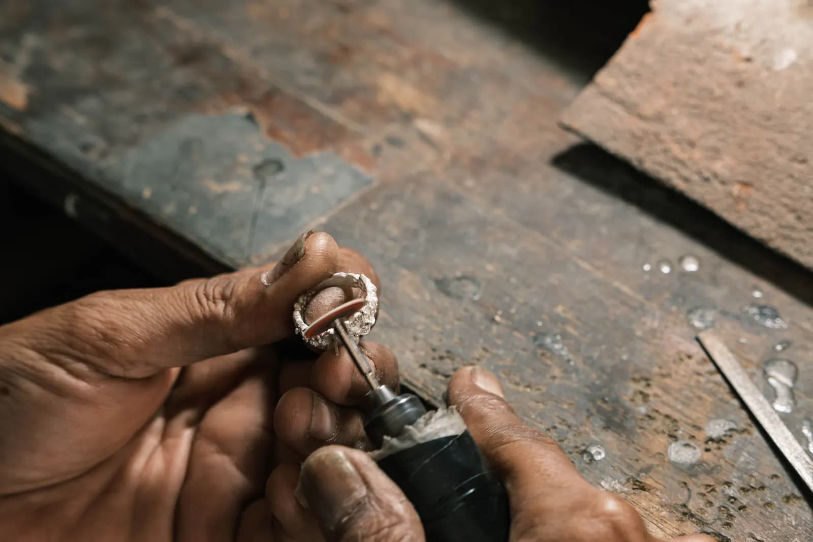 Hands finishing a ring with a rotary tool on a worn bench