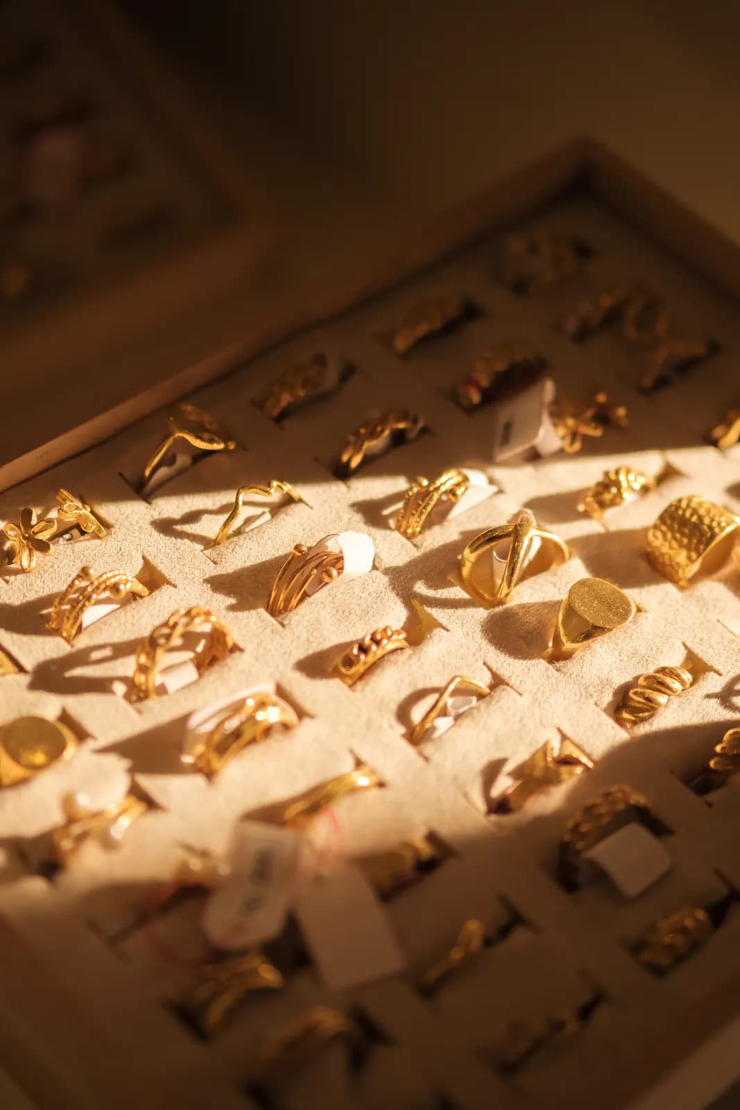 Cream display tray filled with rows of gold rings in warm light