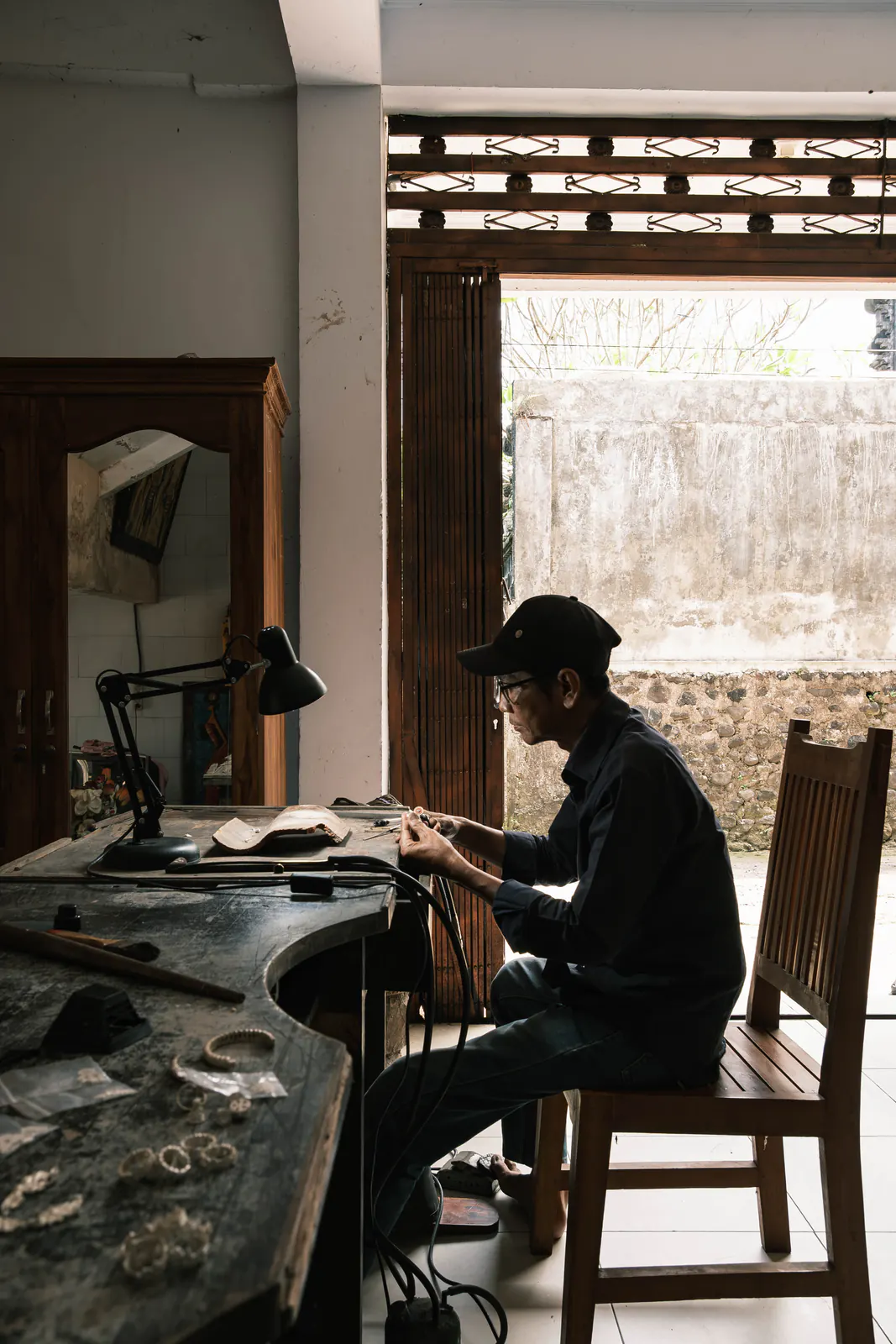 Artisan seated at a curved wooden workbench by an open doorway
