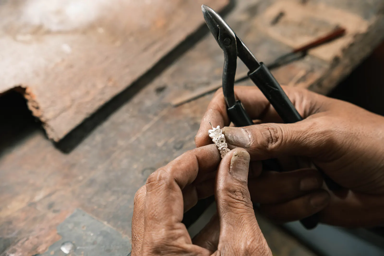 Hands shaping a ring with pliers over a worn bench